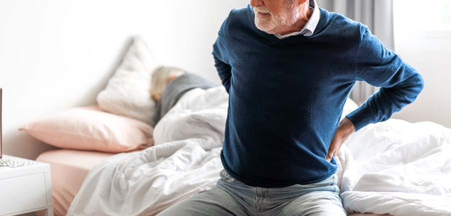 Mann sitzt auf einem Bett und hält sich den Rücken. Liegt ein ISG-Syndrom vor, kommen zunächst konservative Maßnahmen wie Akupunktur, Wärmebehandlung oder Physiotherapie zum Einsatz.