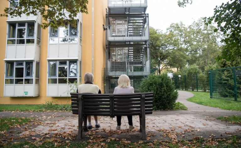 Zwei ältere Frauen sitzen auf einer Bank vor einem Pflegeheim - Vorteilhaft Leben - Vorteilhaft Leben